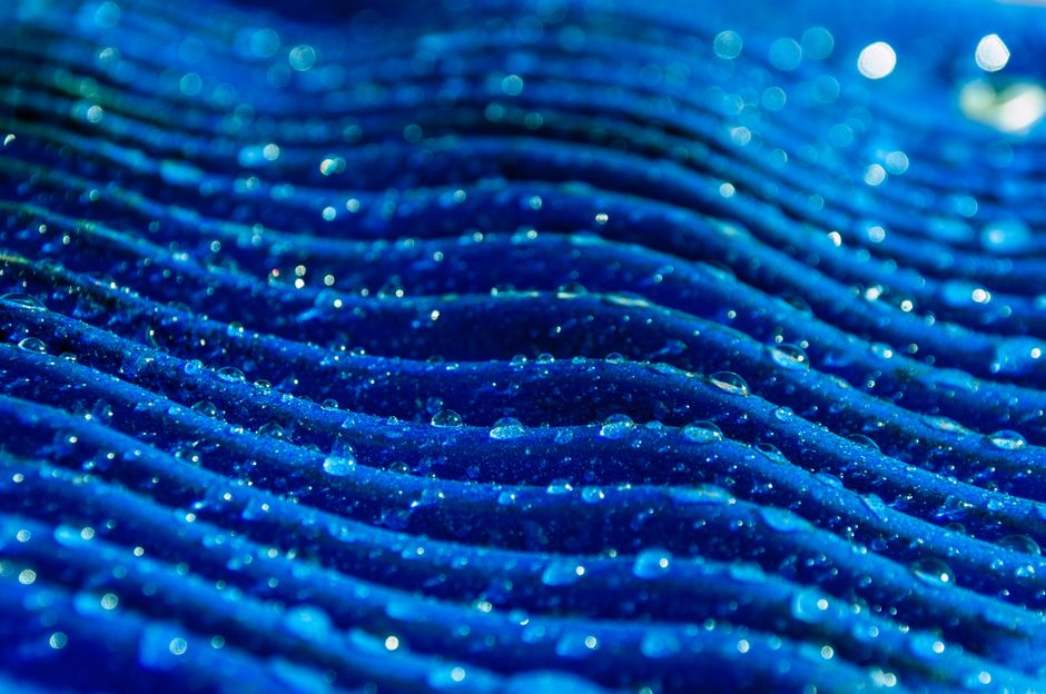 Close-up of water droplets on a vibrant blue textured surface, creating an abstract pattern.