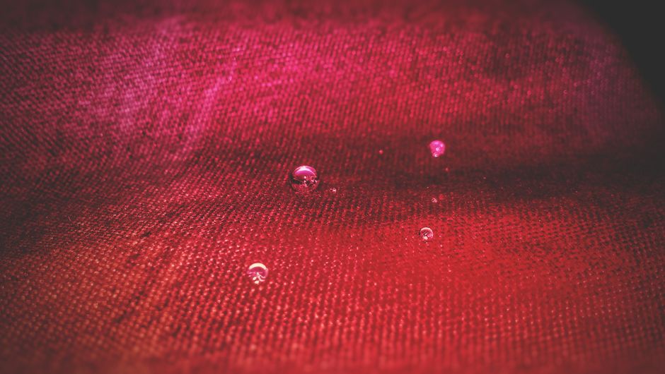 Close-up view of water droplets resting on vibrant red textile surface.
