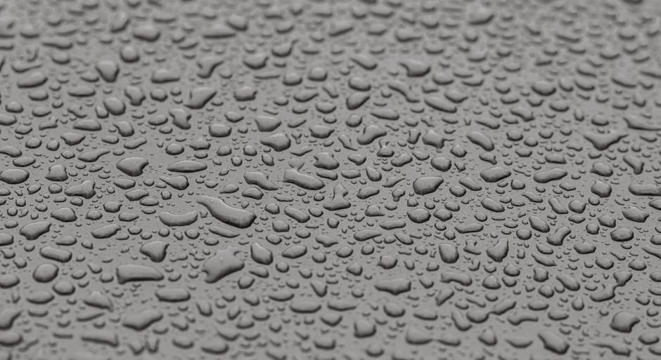 A detailed still-life image of water droplets on a textured gray surface, showcasing texture and contrast.