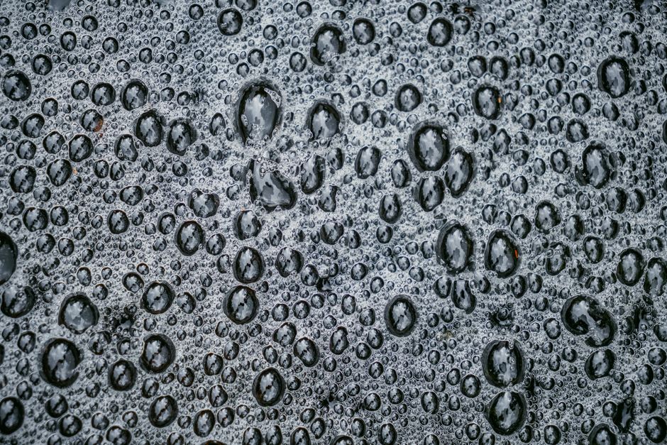Detailed view of water droplets creating a pattern on a dark surface, showcasing natural beauty.